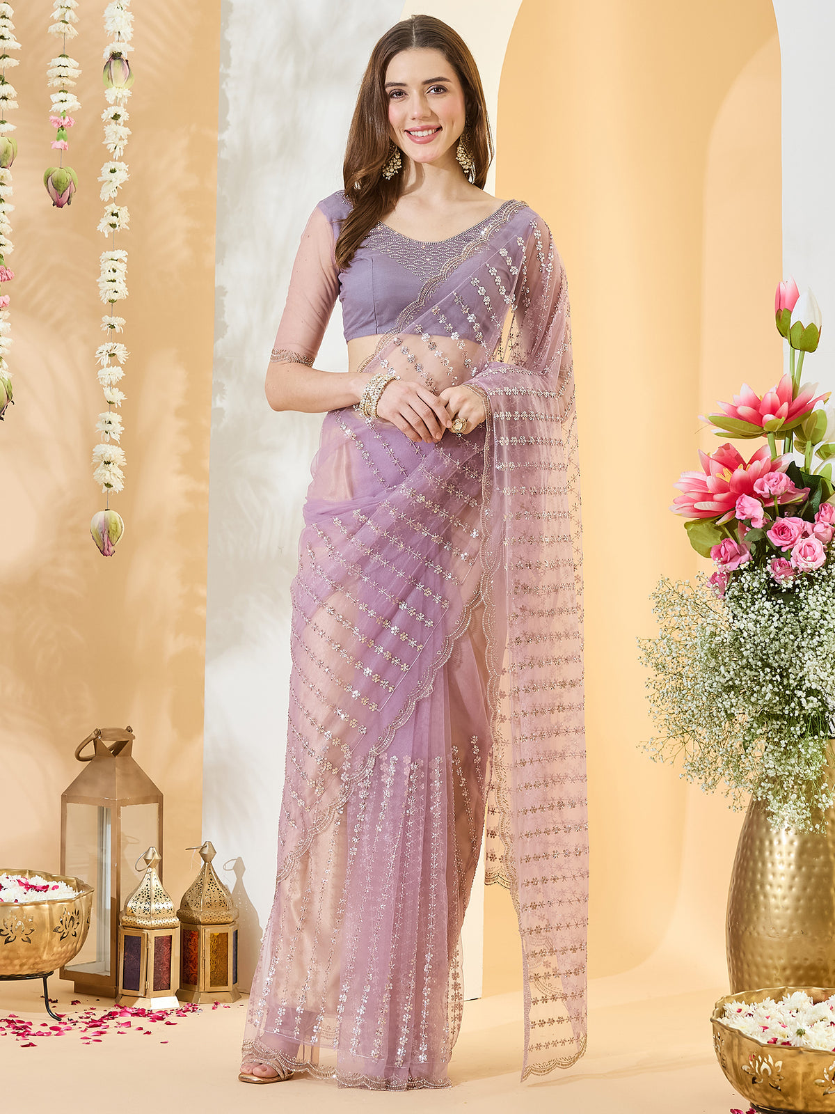 Woman wearing lavender net saree with ornamented surface design and lavender blouse