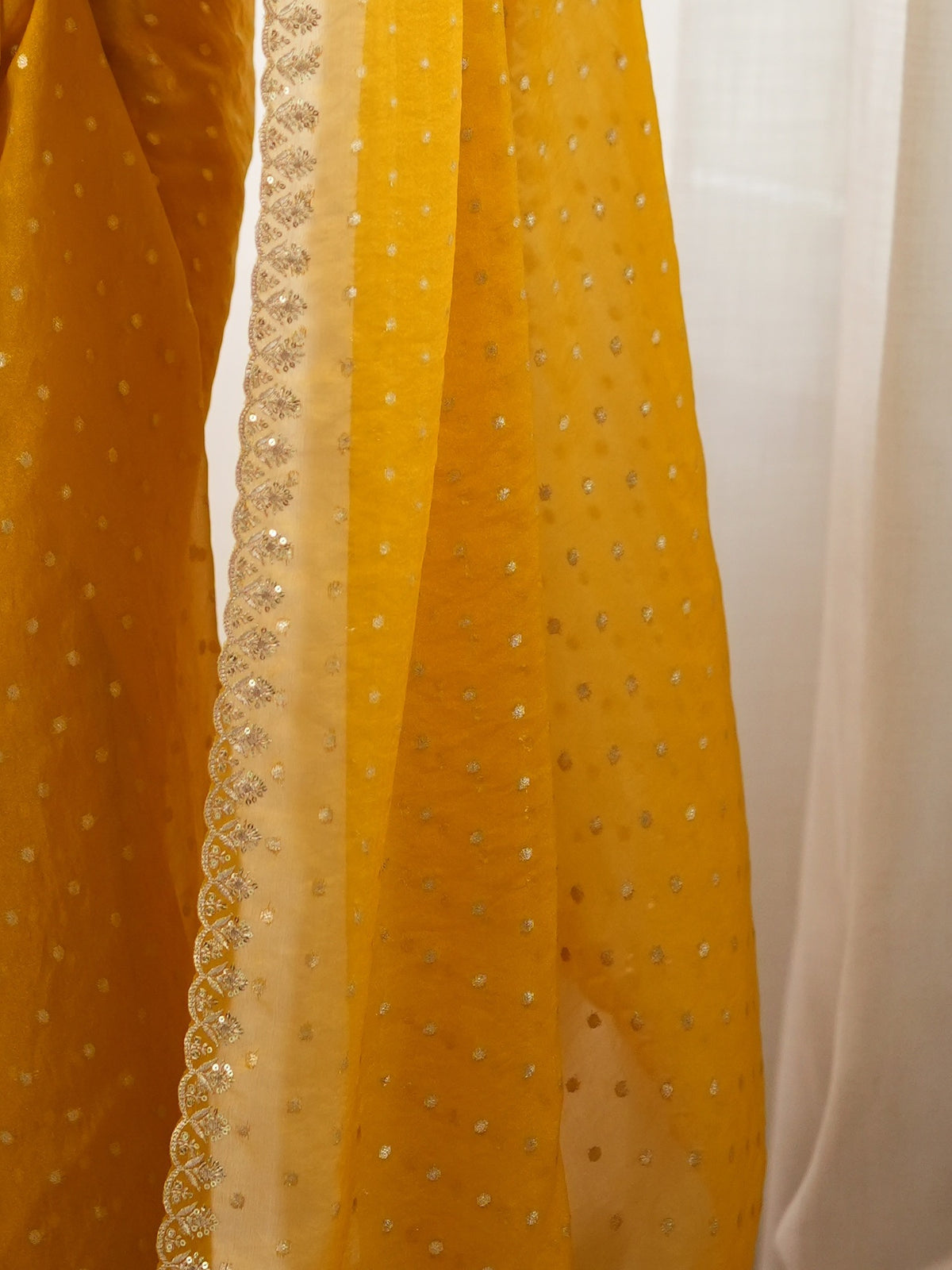 Pallu detail of mustard georgette saree showing zari butta (metallic motif) work and embellished border