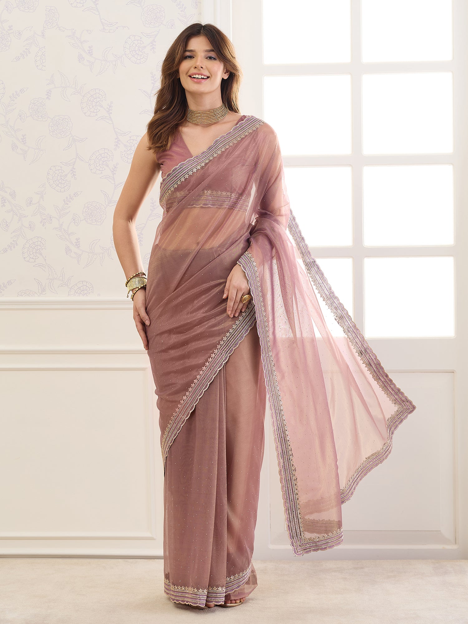 Woman wearing rose gold net saree with ornamented surface design and rose gold blouse