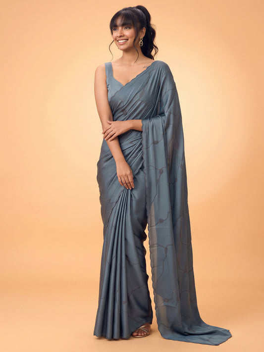 Woman wearing teal blue satin silk saree with ornamented surface design and teal blue blouse