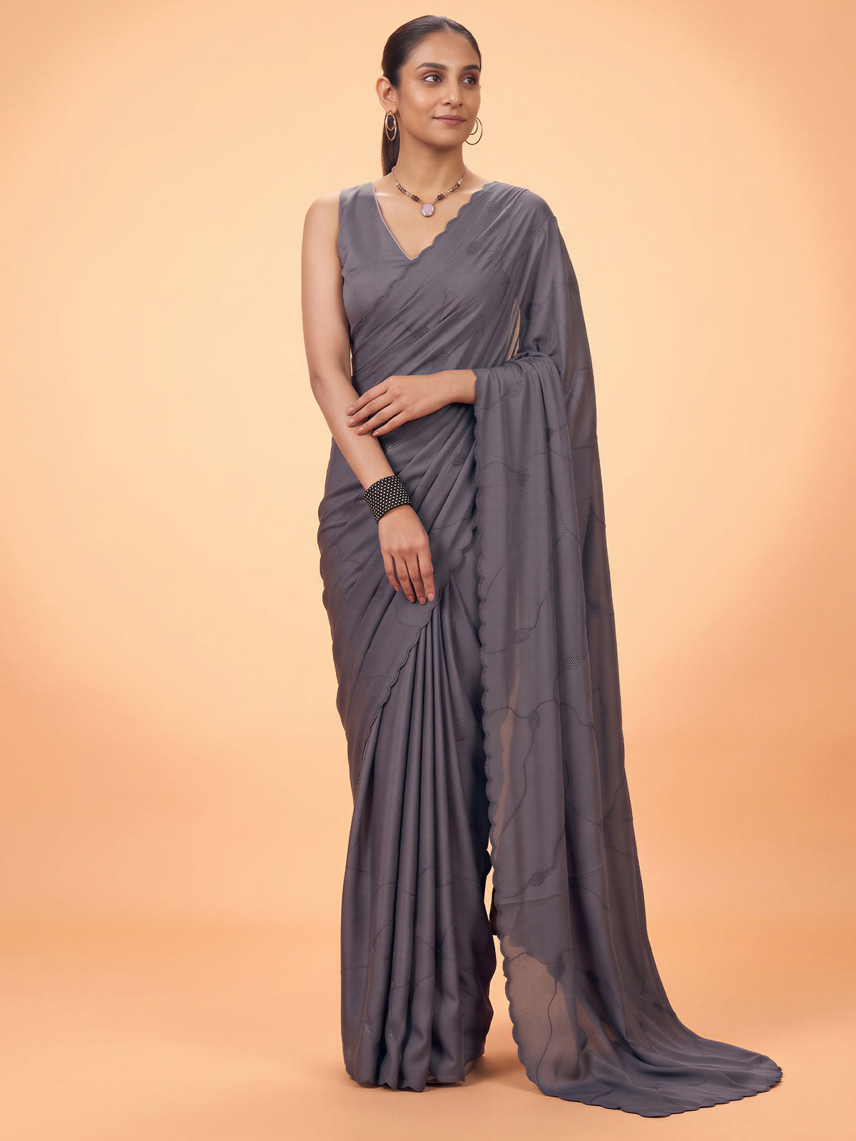 Woman wearing charcoal grey satin silk saree with ornamented surface design and charcoal grey blouse