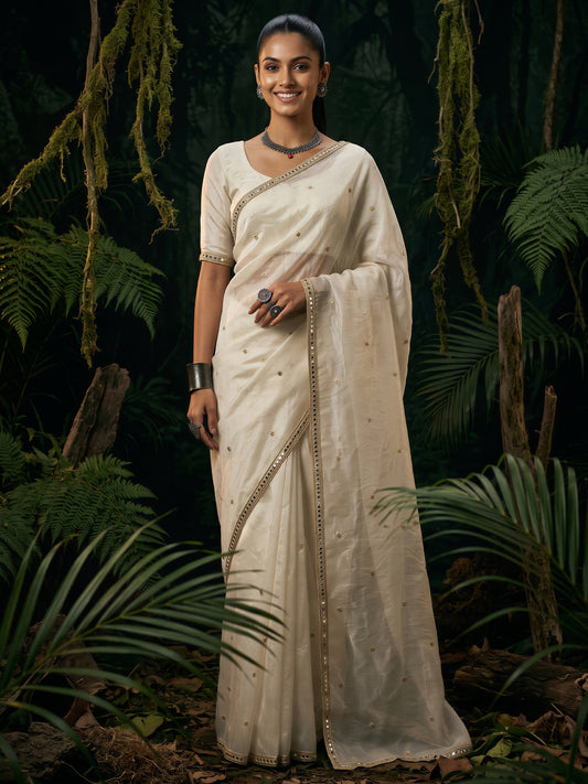 Woman wearing off white satin saree with ornamented surface design and off white blouse