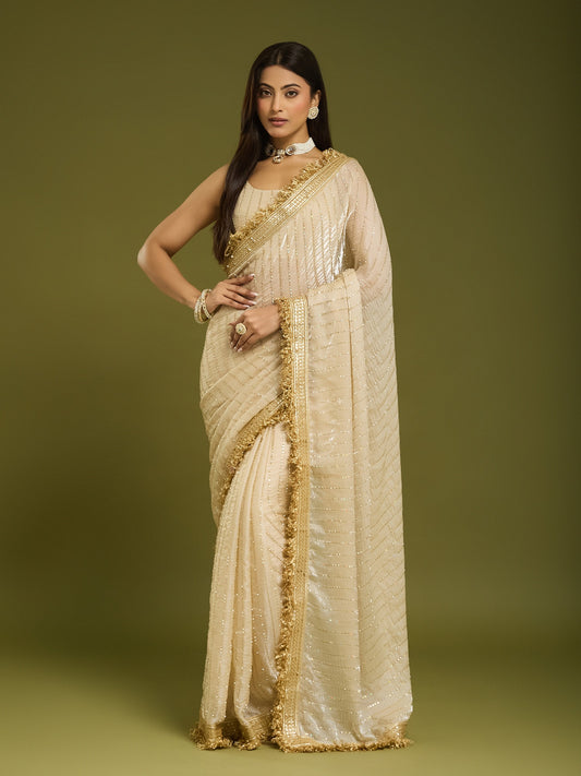 Woman wearing cream satin saree with ornamented surface design and cream blouse
