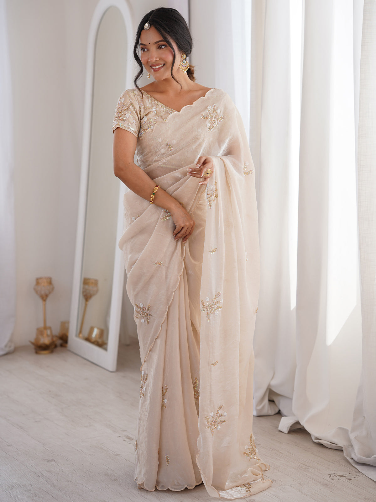 Woman wearing off white satin saree with ornamented surface design and off white blouse
