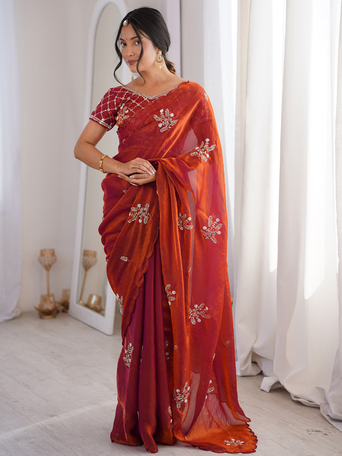 Woman wearing rust satin saree with ornamented surface design and rust blouse