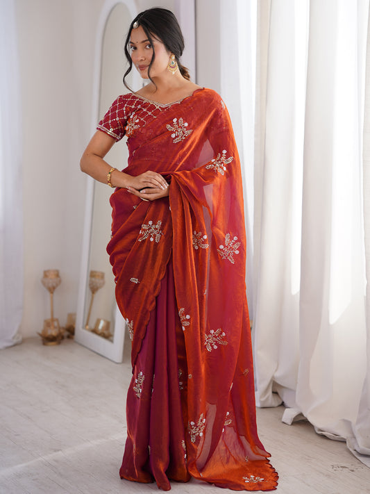 Woman wearing rust satin saree with ornamented surface design and rust blouse