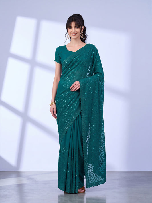 Woman wearing teal green tissue saree with ornamented surface design and teal green blouse