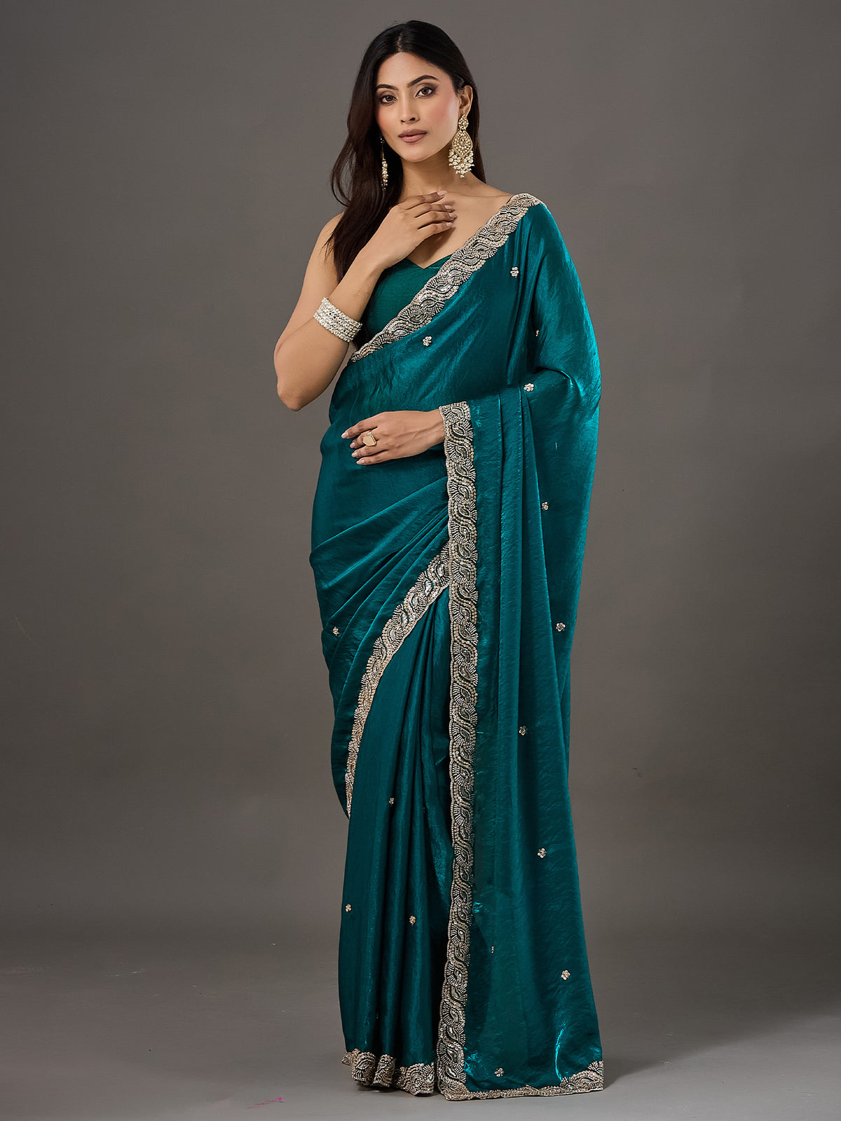 Woman wearing teal green satin saree with ornamented surface design and teal green blouse