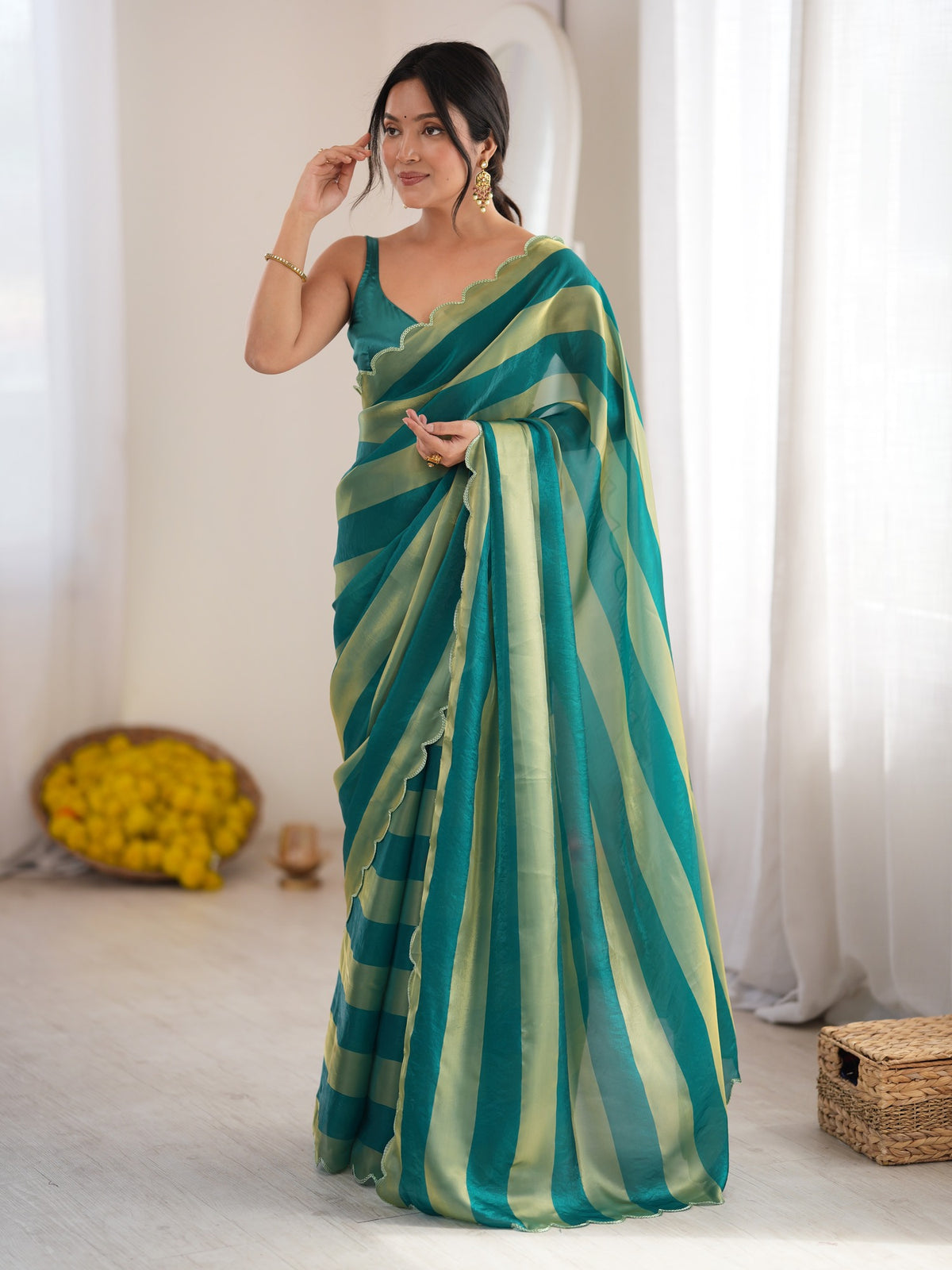 Woman wearing teal green satin saree with striped pattern design and teal green blouse