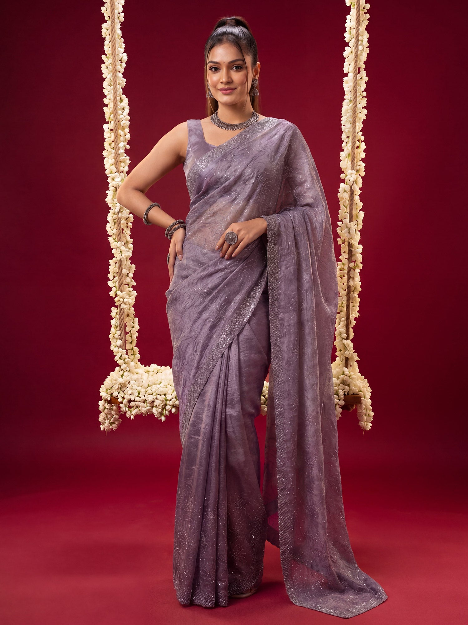 Woman wearing lavender tissue saree with ornamented surface design and lavender blouse