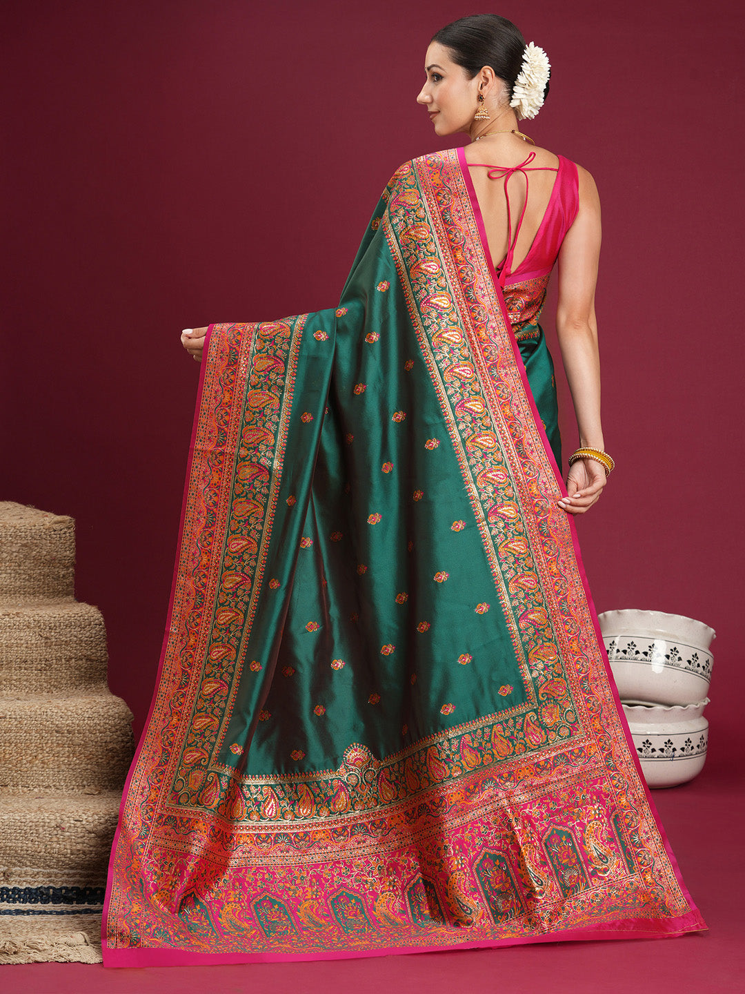 Back pose of model in teal green Banarasi silk saree showing rani pink pallu draped over arm with paisley motifs