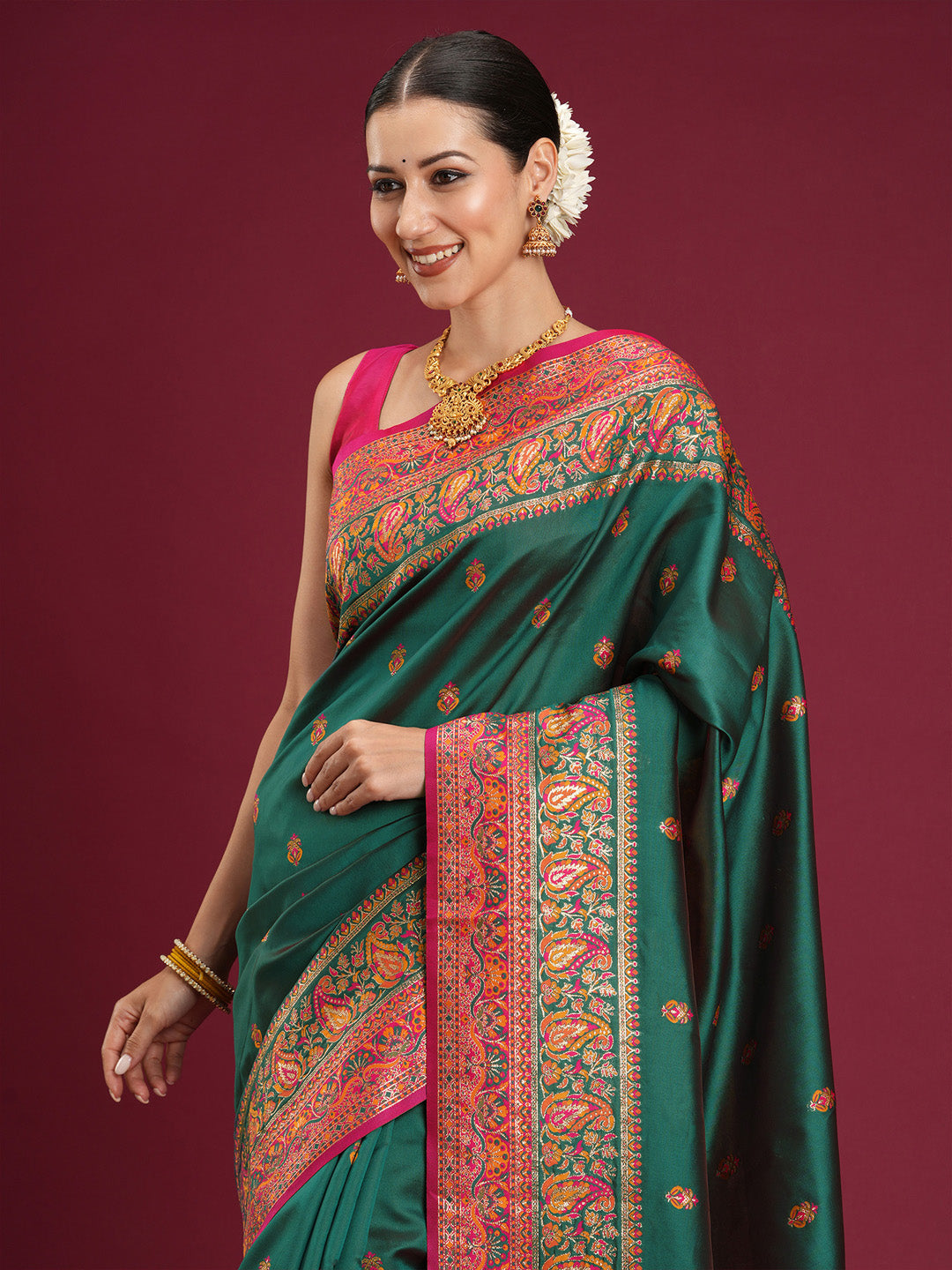 Side pose of model in teal green Banarasi silk saree showing rani pink border and pallu with paisley and floral motifs