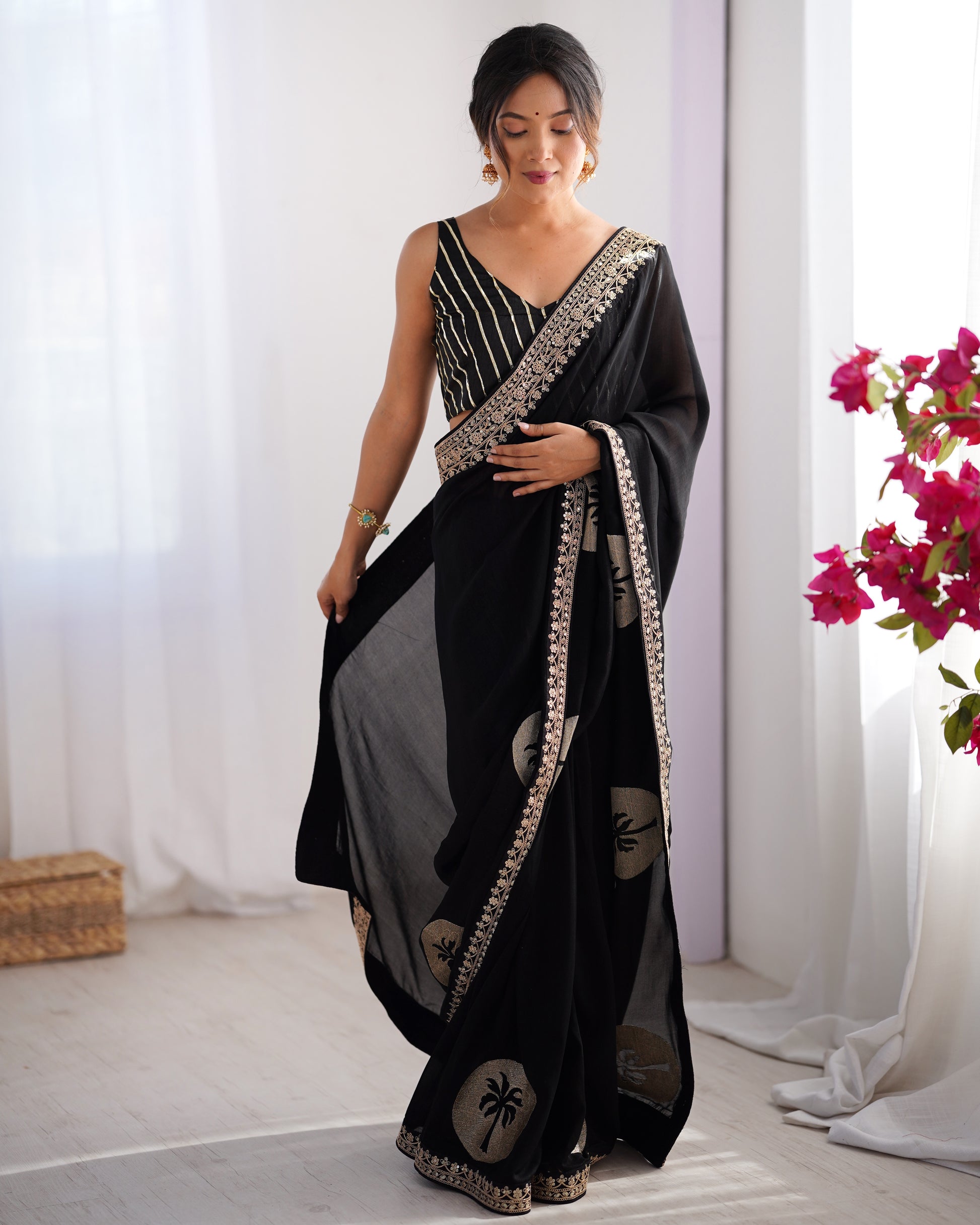 Woman wearing a black saree with white patterns in a bright room.